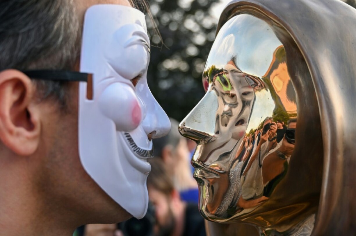 Un homme portant un masque de Guy Fawkes face à une statue en bronze en hommage à Satoshi Nakamoto, le pseudonyme du mystérieux inventeur de la cryptomonnaie Bitcoin, le 16 septembre 2021 à Budapest, en Hongrie
