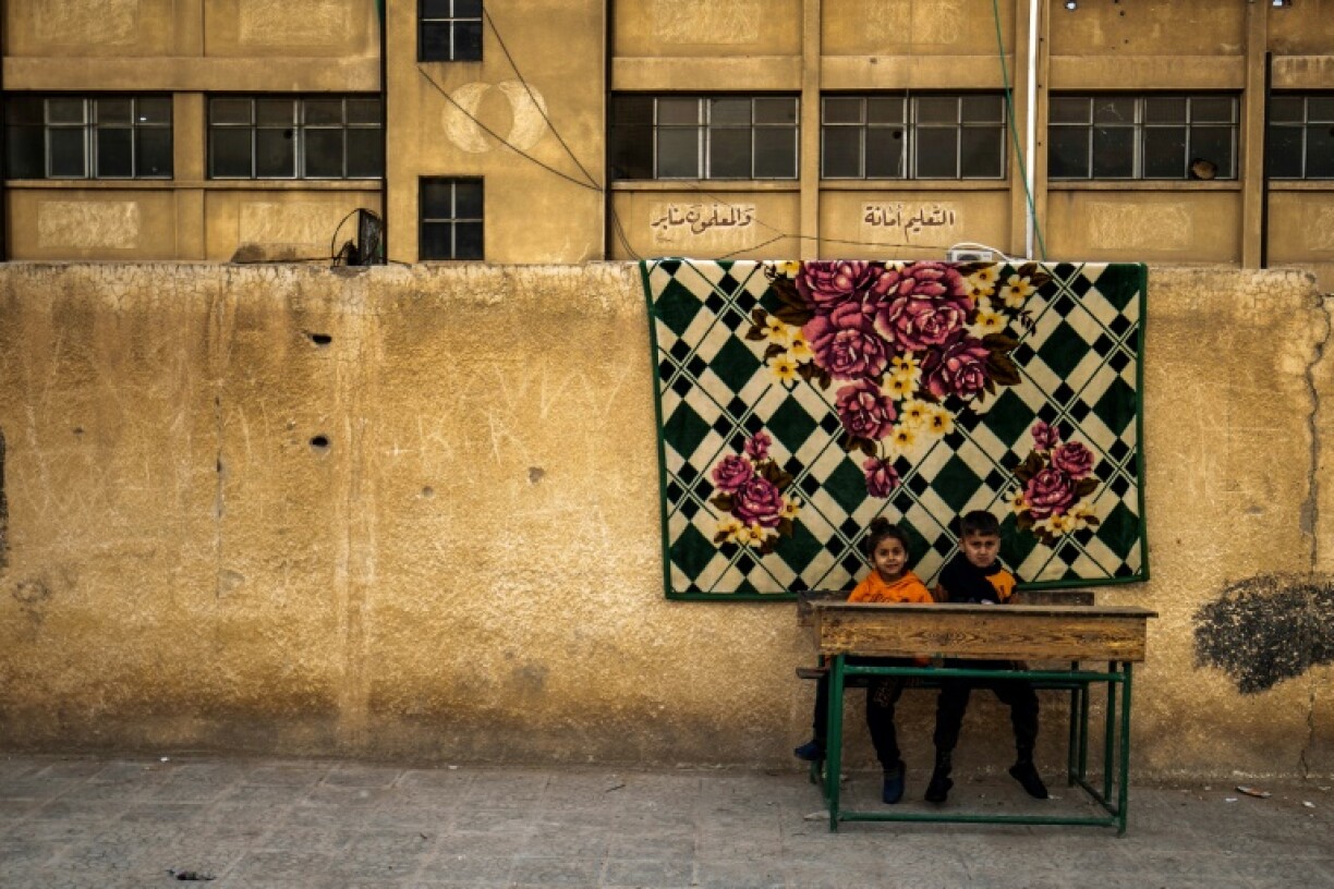 Children who fled ongoing battles between Turkish-backed groups and Syrian Kurdish forces in Syria's Aleppo province sit at a desk in the yard of a school in Hasakeh, where they and others took refuge
