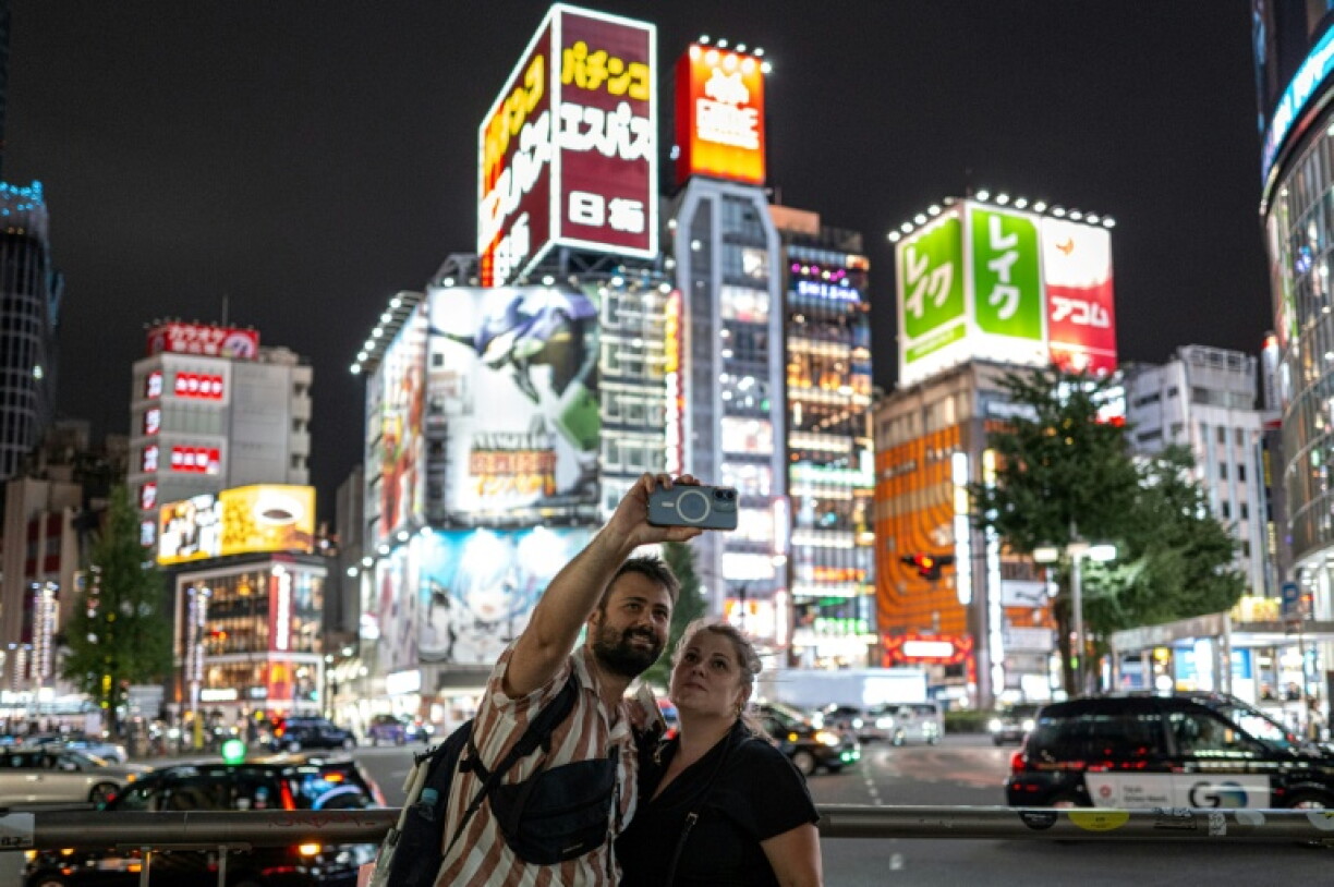 Des touristes font un selfie dans le quartier de Shinjuku, le 11 août 2026 à Tokyo