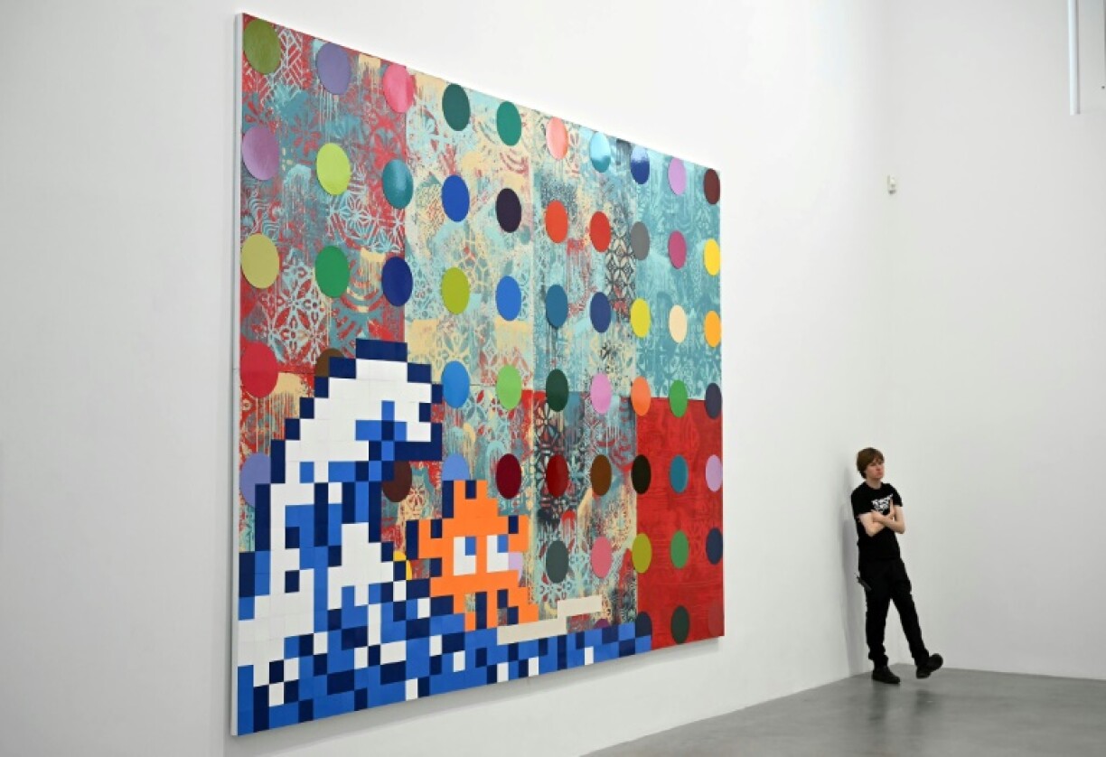 A gallery assistant stands next to the artwork 'Troubled Waters', 2025, by US artist Shepard Fairey, British artist Damien Hirst, and French street artist Invader