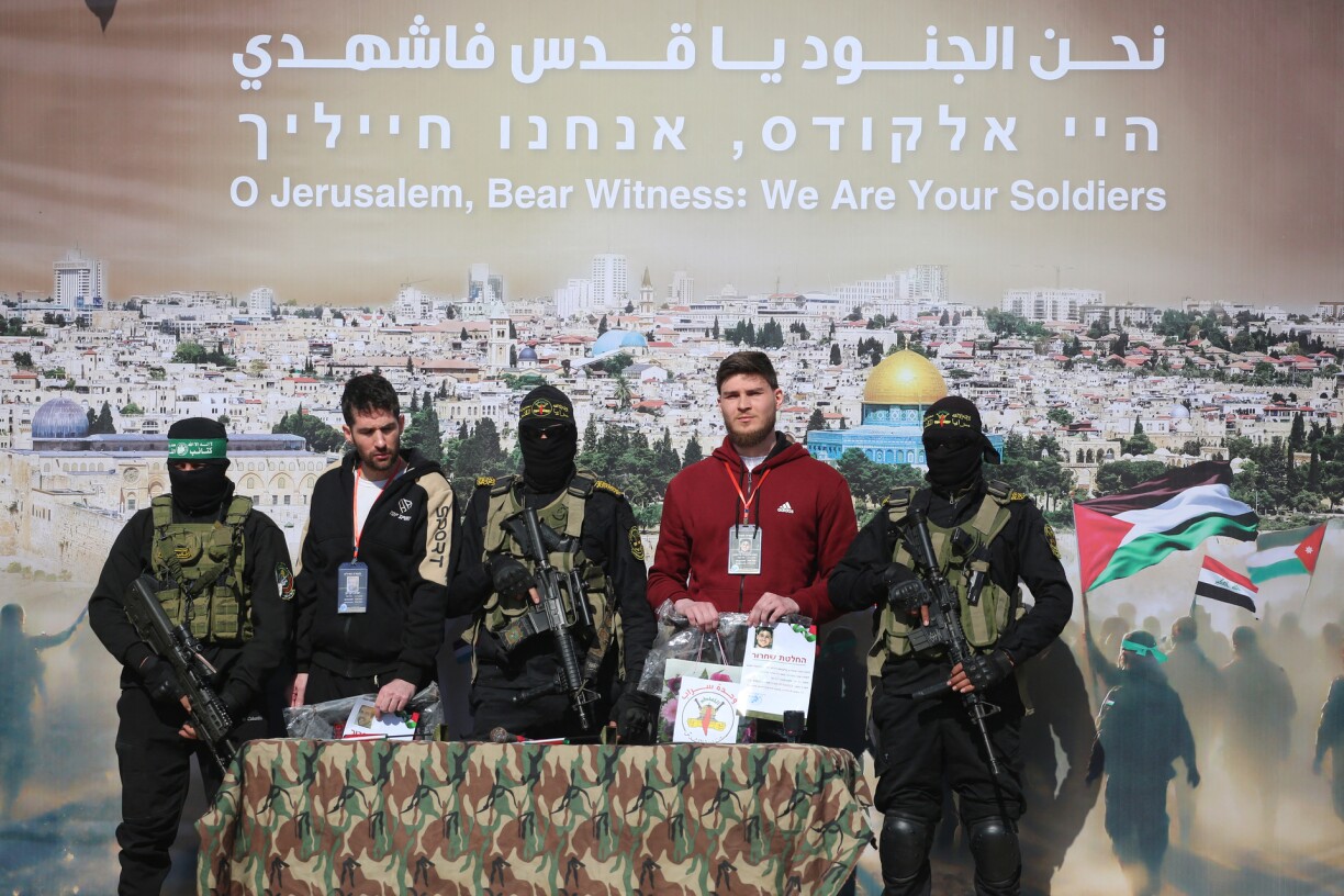 Israeli-Argentinian hostage Yair Horn (L) and Israeli-Russian Sasha Trupanov (R) stand on stage next to Palestinian militatns during their handover over to a Red Cross team in Khan Yunis in the southern Gaza Strip on February 15, 2025, as part of the sixth hostage-prisoner exchange.