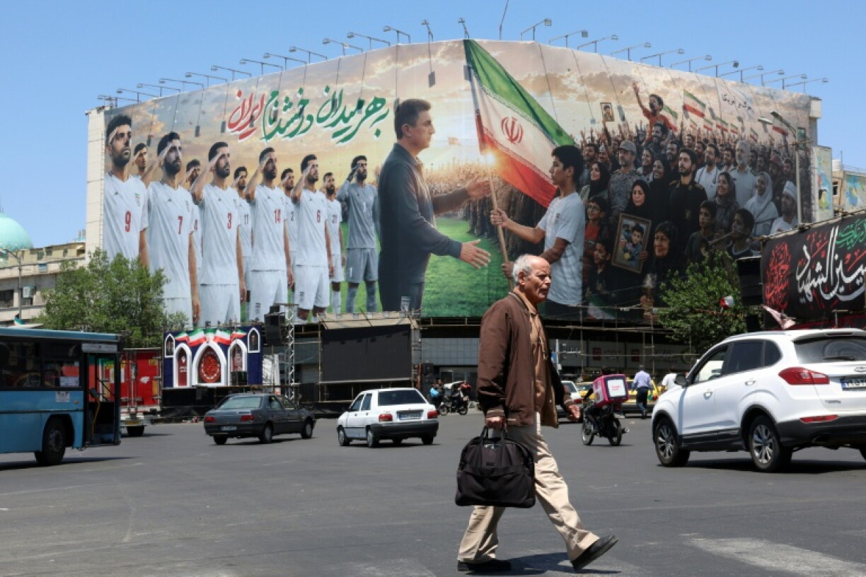 Un Iranien passe devant un panneau d'affichage géant mettant en scène l'équipe nationale iranienne de football qui a pris la direction de la Turquie pour y préparer le Mondial-2026, le 18 mai 2026 à Téhéran