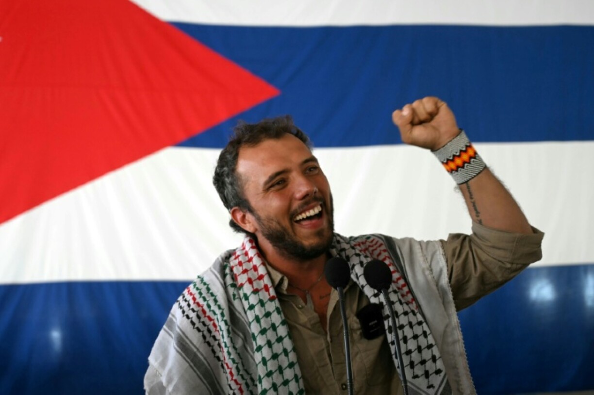 L'activiste brésilien Thiago Avila lève le poing et sourit devant un drapeau cubain après son arrivée au port de La Havane à bord du bateau de pêche Maguro, faisant partie de la flottille d'aide humanitaire, le 24 mars 2026