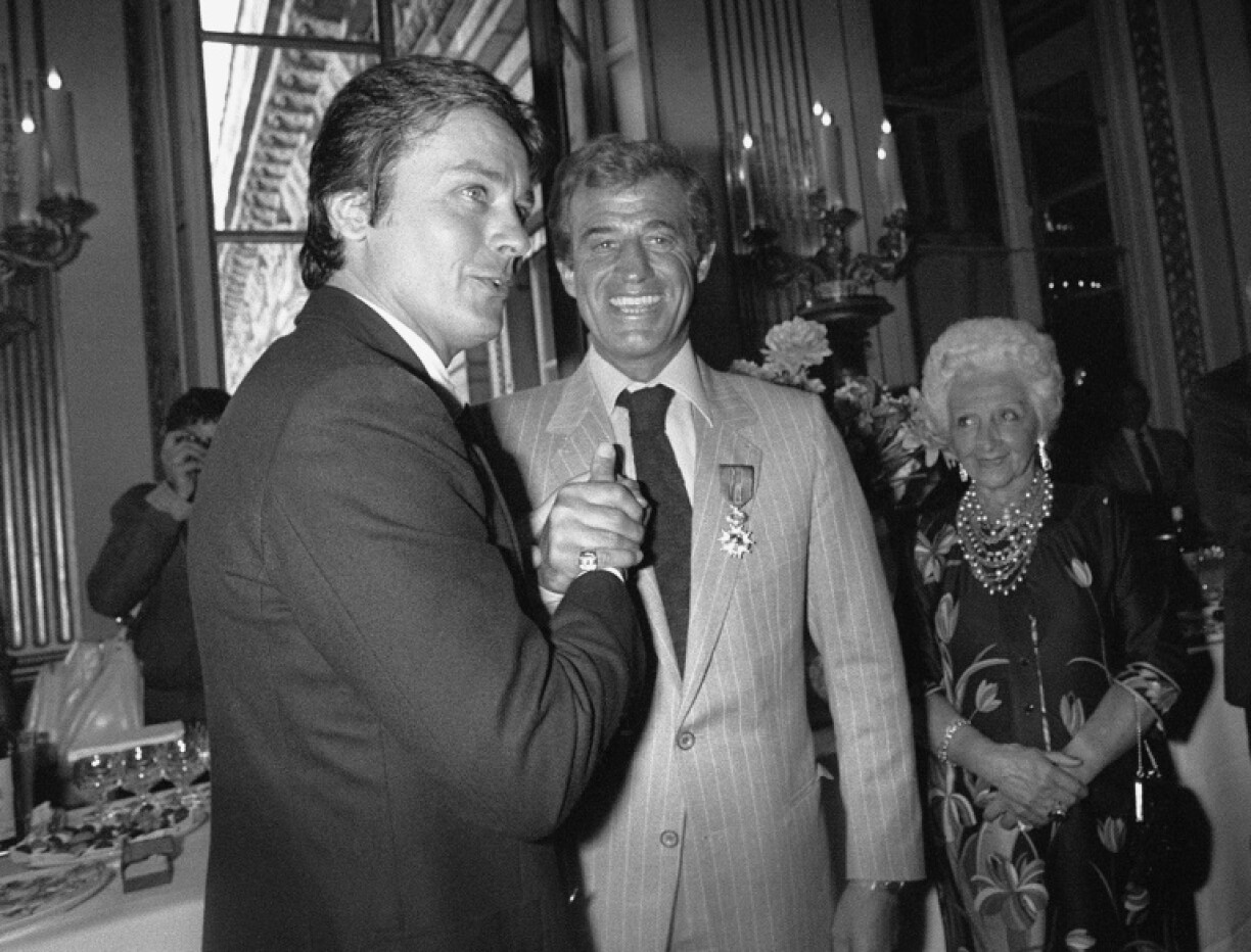 Alain Delon (à gauche) et Jean-Paul Belmondo (à droite) se serrent la main, lors de la remise de la Légion d'honneur à ce dernier, le 23 septembre 1980 à Paris