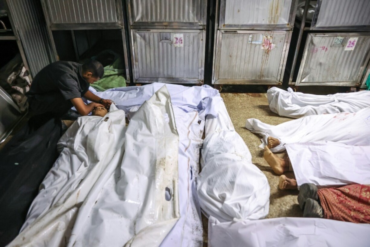 A Palestinian man at the morgue of at Al-Shifa hospital in Gaza City mourns over the shrouded body of a loved one killed while seeking aid near Zikim in the northern Gaza Strip