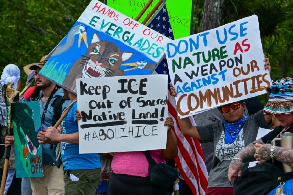 Demonstrators hold signs as they protest US President President Donald Trump's visit