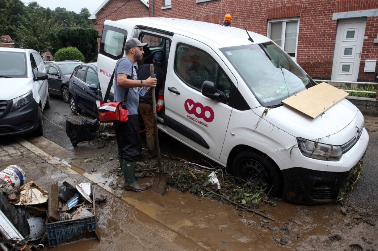 Two men clean up a car piled up after the floods caused major damage in Theux, near Liege, on July 16, 2021. The death toll in Belgium jumped to 23 with more than 21,000 people left without electricity in one region.