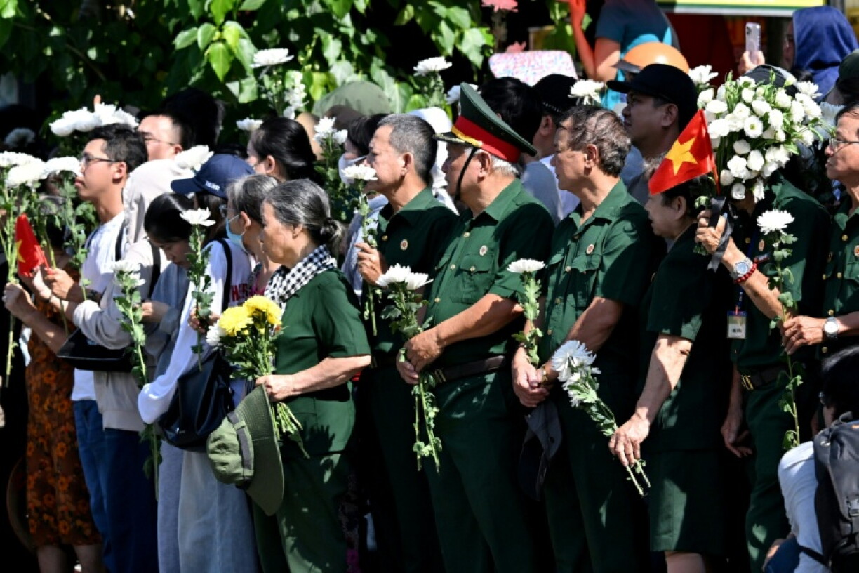People gather with flowers by a roadside as they wait for the vehicles transporting the remains of fallen soldiers to pass by in Ho Chi Minh City