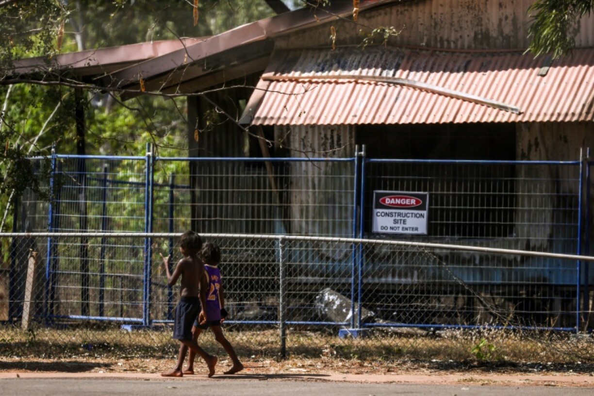 Children walk past a damaged home in Binjari, a remote Indigenous community in Australia's Northern Territory