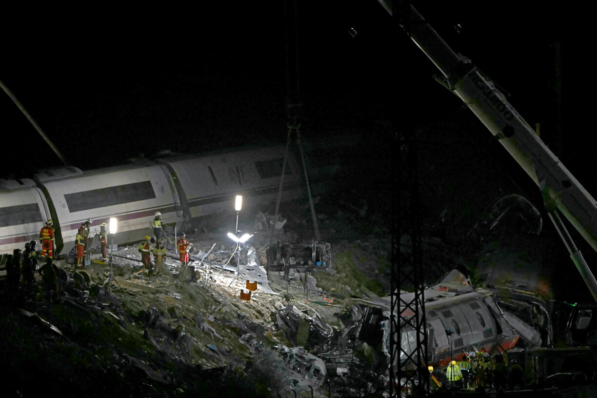 Des membres des services de secours travaillent aux abords d’un wagon transpercé par un rail, sur les lieux de la collision entre deux trains à grande vitesse.