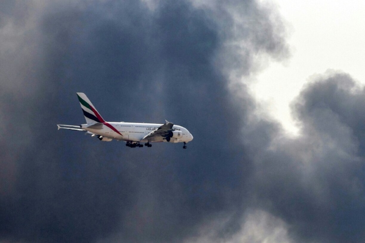 Un Airbus A380 d'Emirates se prépare à atterrir à l'aéroport de Dubaï d'où s'élève une épaisse fumée noire d'un incendie, le 16 mars 2026 aux Emiras arabes unis
