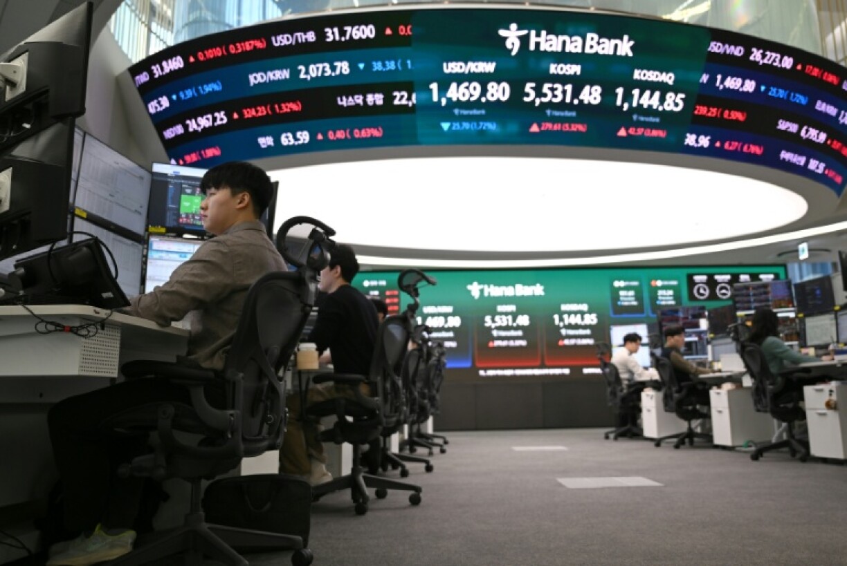 Des cambistes surveillent les taux de change tandis qu'un écran électronique affiche les indices boursiers de référence dans une salle des marchés des changes de la Hana Bank à Séoul, le 10 mars 2026 en Corée du Sud