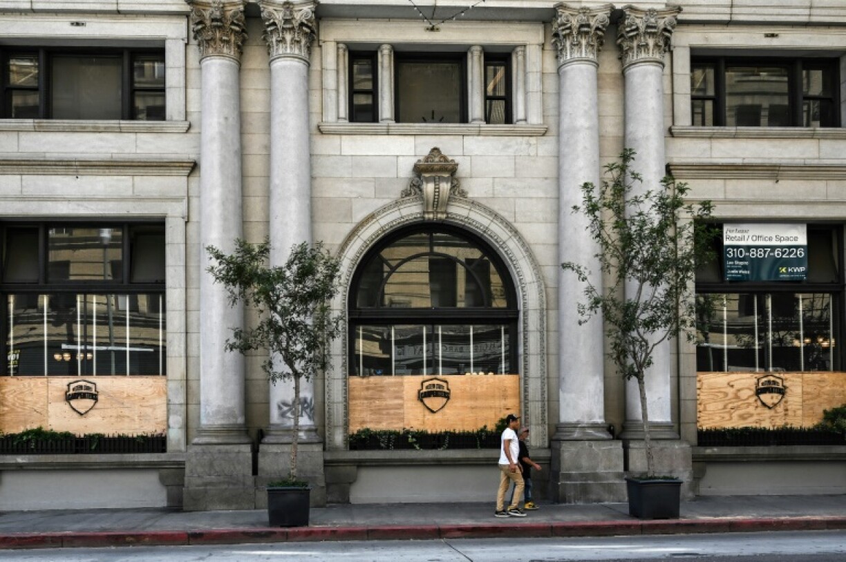 People walk past plywood covering the windows of a building in downtown Los Angeles on June 11, 2025