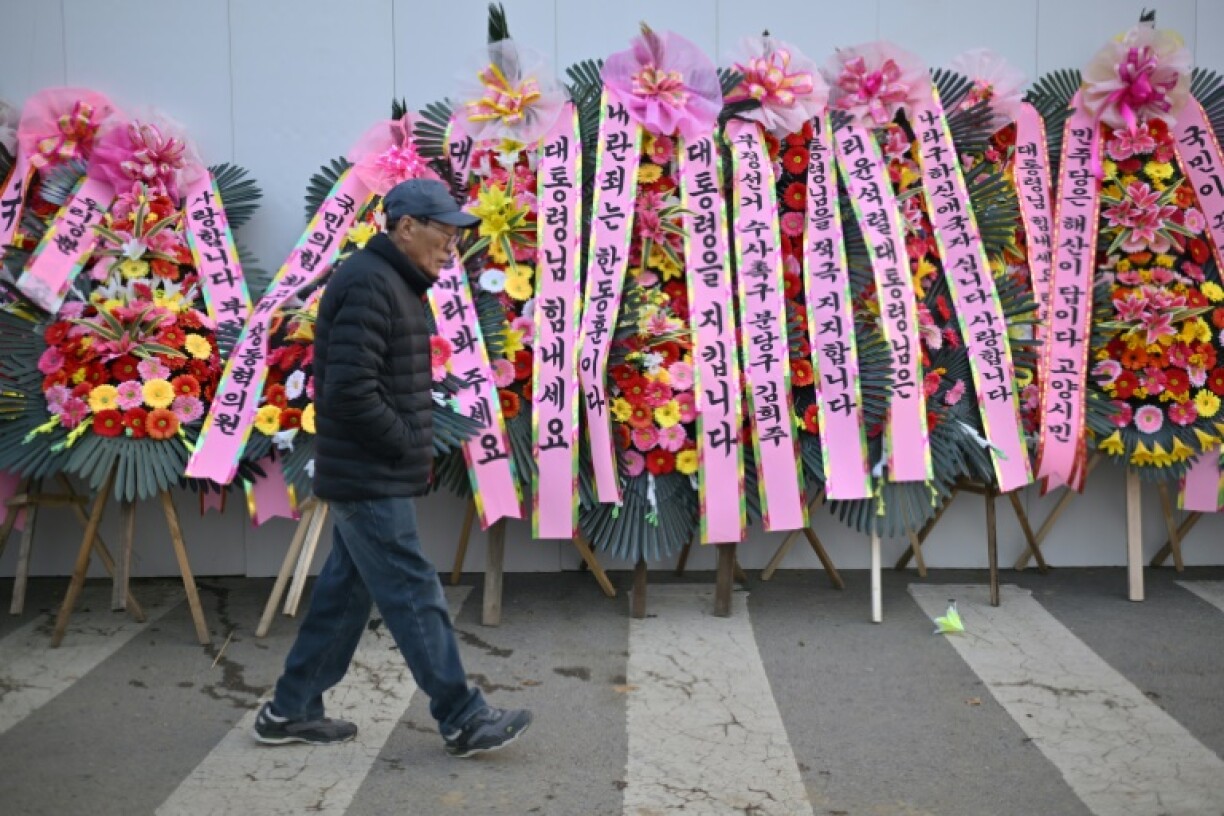A man walks past flowers displayed in support of South Korean President Yoon Suk Yeol outside his office in Seoul