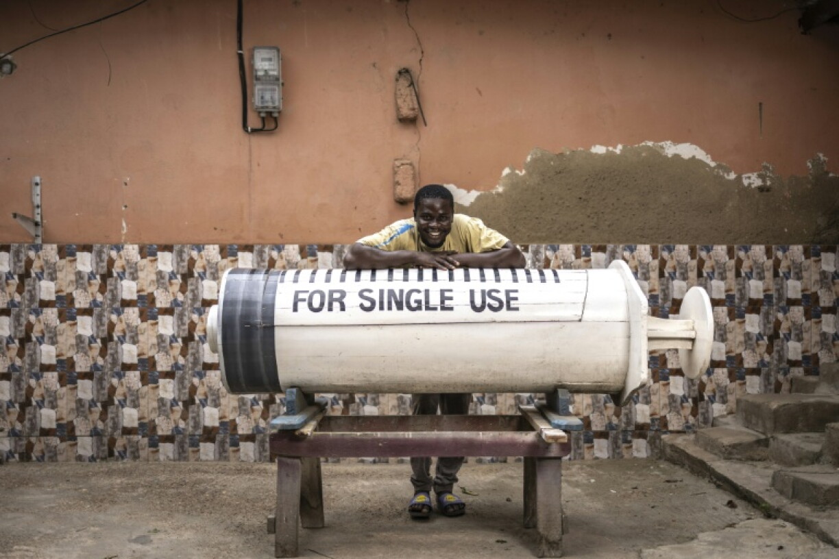 Lawrence Anang, fabricant de cercueils âgé de 26 ans, pose pour une photo avec un cercueil en forme de seringue, conçu en référence à la profession du défunt, un médecin, près de l’atelier de menuiserie Kane Kwei à Accra, au Ghana, le 17 août 2026