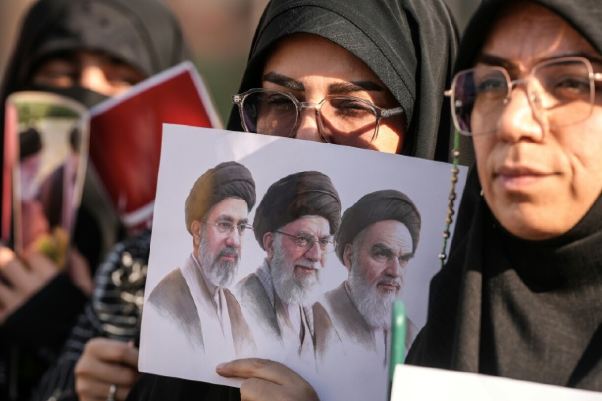 Des personnes en deuil tiennent une une photo du défunt fondateur de la République islamique, l'ayatollah Khomeini, du guide suprême défunt, l'ayatollah Khamenei, et de l'actuel guide suprême, Mojtaba Khamenei, lors du cortège funèbre de l'ayatollah Ali Khamenei à Nadjaf, le 8 juillet 2026 en Irak