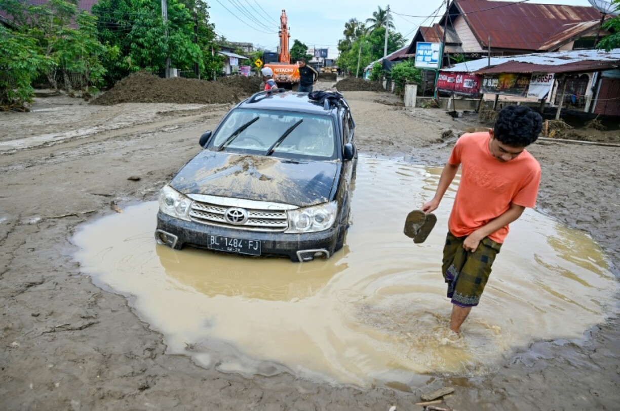 Un homme passe devant une voiture embourbée à la suite de crues soudaines à Meureudu, dans la province d’Aceh, en Indonésie, le 28 novembre 2025