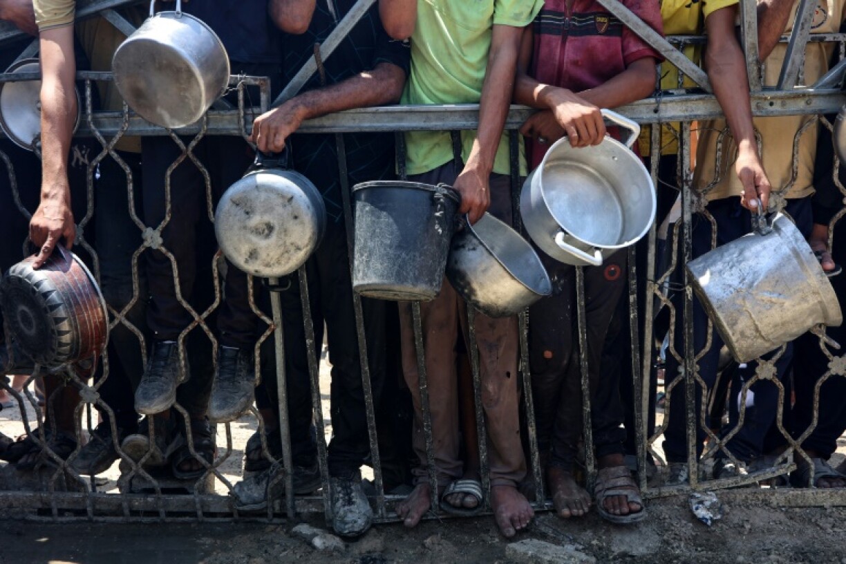 Palestinians carry empty pots as they wait to receive lentil soup at a food distribution point in Gaza City on August 2, 2025