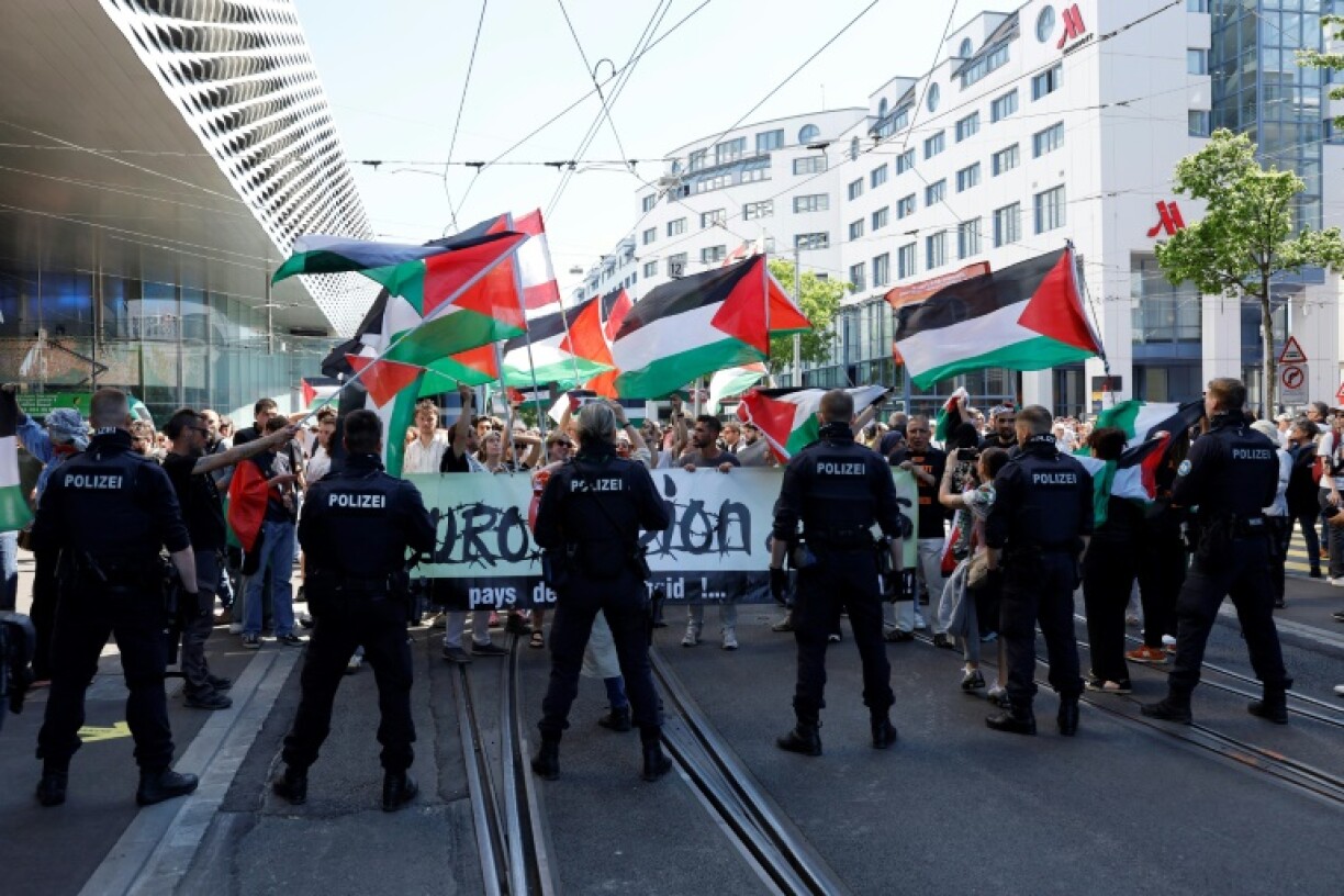 Police officers stand guard in front of protesters waving Palestinian flags during the Eurovision opening ceremony