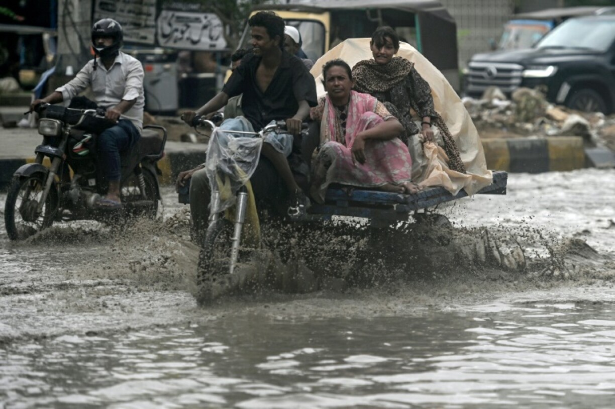 Commuters make their way through a flooded street after heavy rainfall in Karachi
