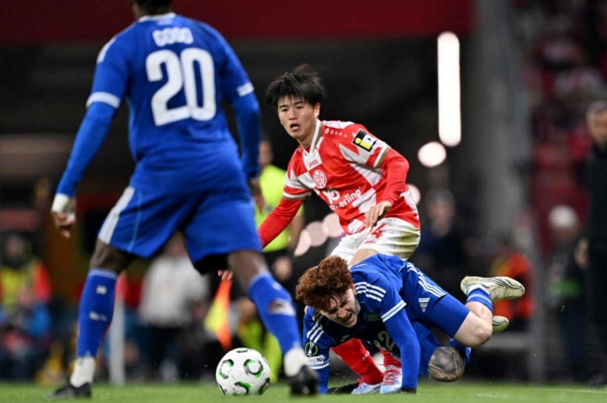Le milieu japonais de Mayence Sota Kawasaki (C) et l'Argentin de Strasbourg Valentin Barco (à terre) lors de la défaite des Alsaciens 2 à 0 en quart de finale aller de Ligue Conférence, le 9 avril 2026 à Mayence