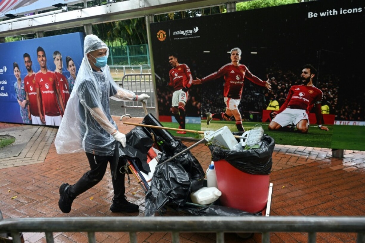 A man pushes a rubbish bin past posters of Manchester United players outside Hong Kong Stadium