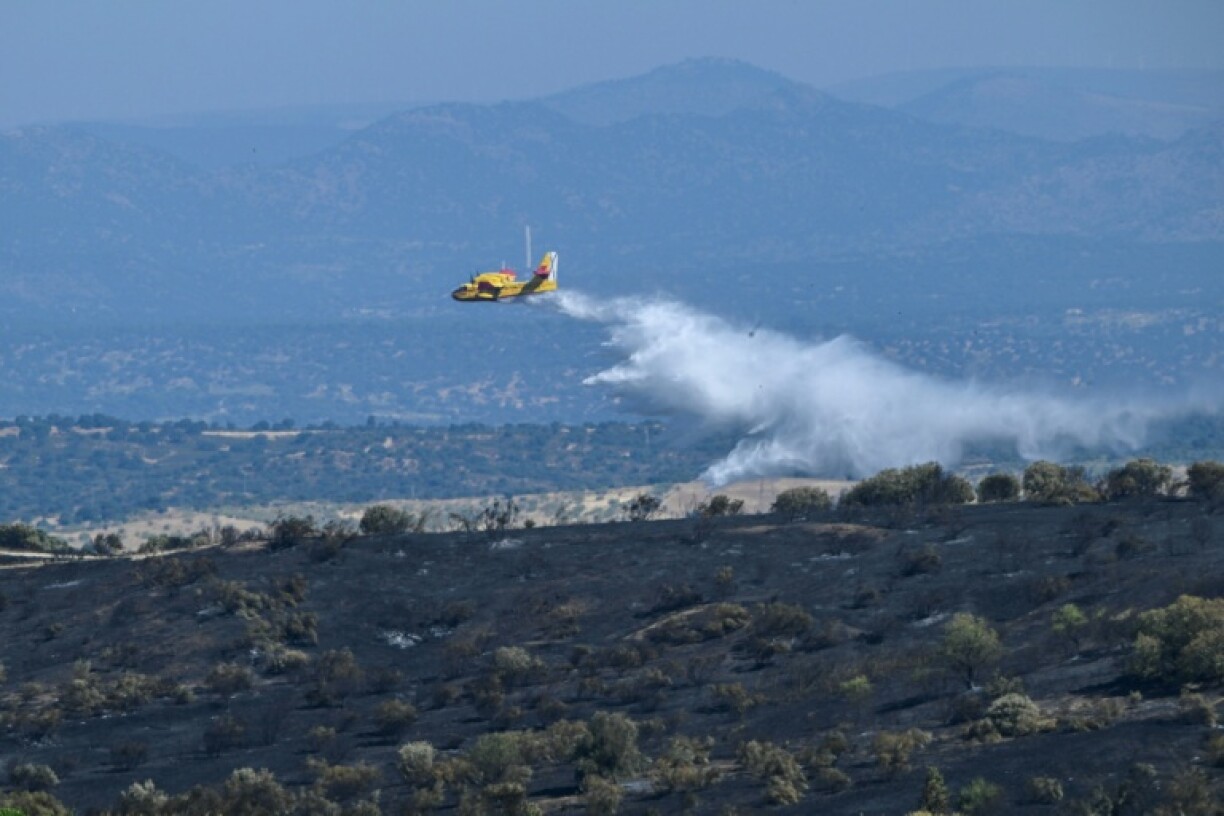 A firefighting airplane releases water over burnt areas following a wildfire which started in the municipality of Mentrida