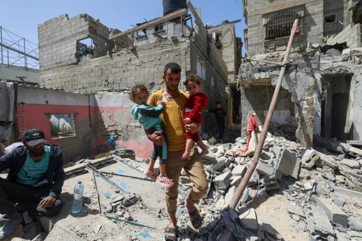 A Palestinian man carries children across the rubble of a house that was destroyed in an Israeli air strike in Khan Yunis