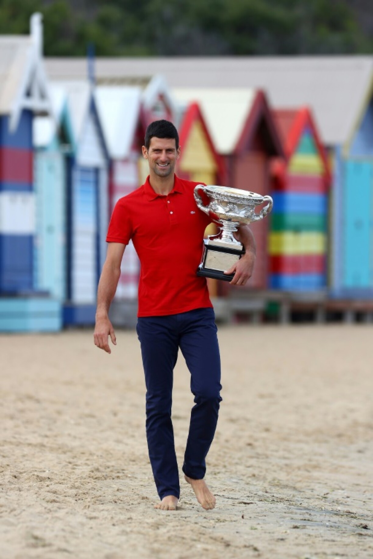 Le Serbe Novak Djokovic pose pour les photographes sur la plage de Brighton Beach de Melbourne le 22 février 2021, avec son trophée obtenu la veille à l'Open d'Australie