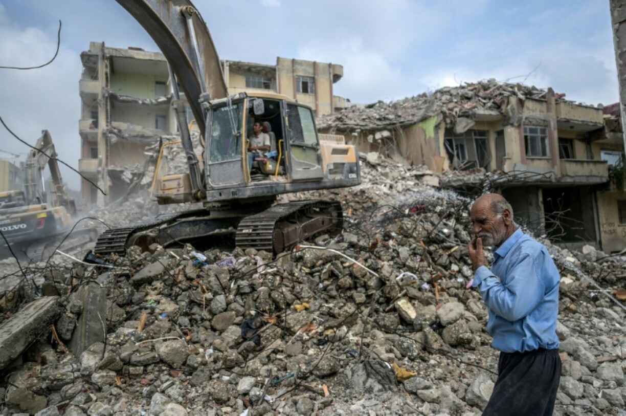 Un homme passe devant une pelleteuse nettoyant les gravats d'un bâtiment détruit, le 9 juillet 2023 à Samandag, en Turquie