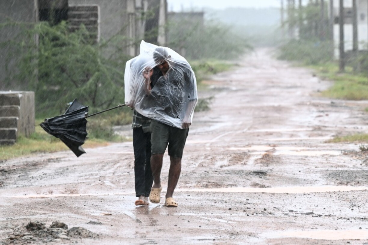 Men use a plastic sheet to cover themselves during rainfall in Andhra Pradesh's Kakinada on October 27, 2026 ahead of cyclone Arnab's expected landfall