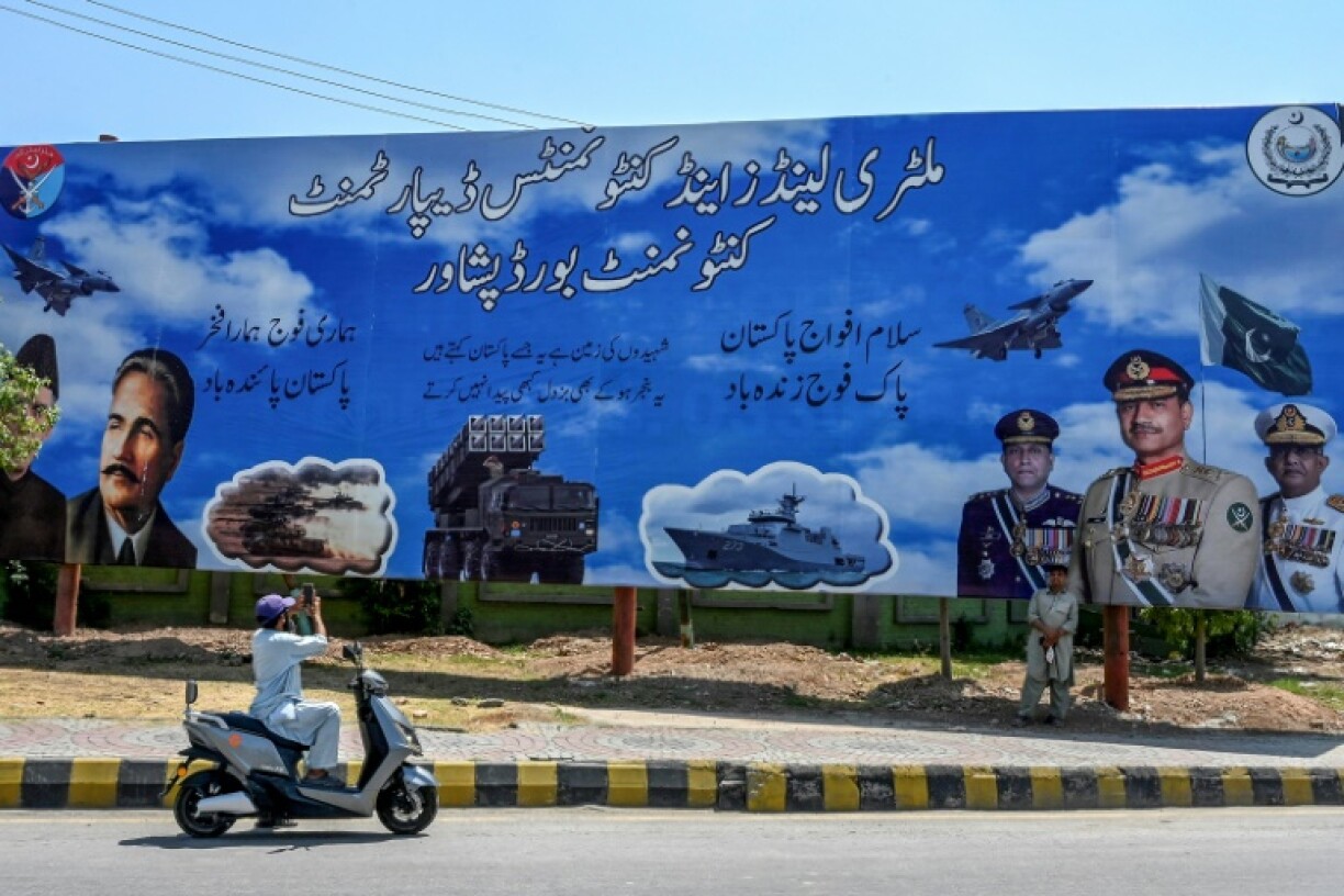 A motorcylist takes a photo of a billboard featuring the heads of Pakistan's navy, air force and army in Peshawar