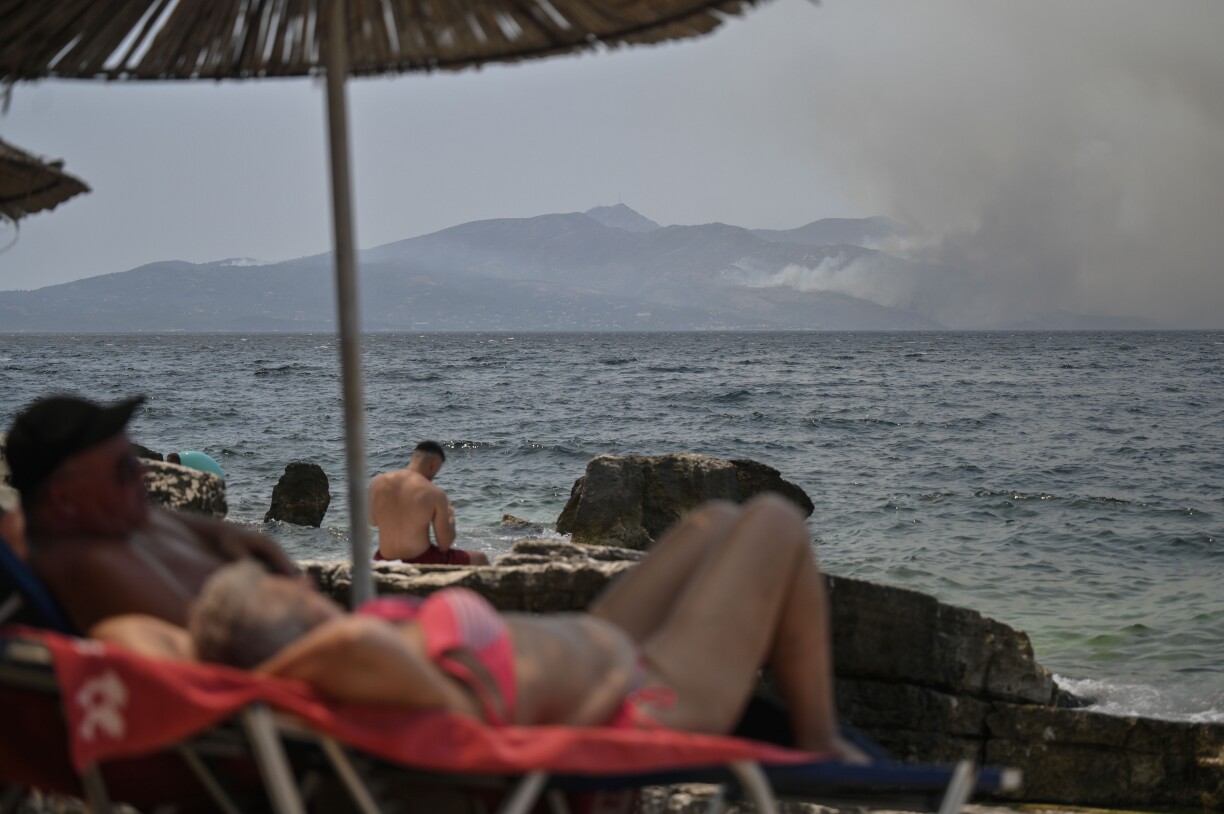 People sunbath near the coastal town of Saranda as smoke billows from the Greek Island of Corfu