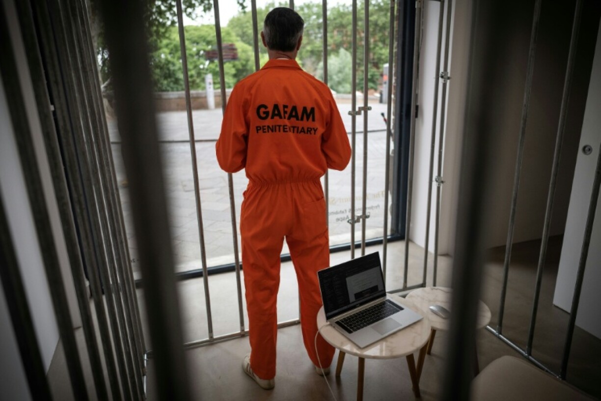 L'artiste Damien Aspe pose derrière la vitrine de sa galerie, debout dans une cage où il s'est enfermé pour dénoncer l'emprise des GAFAM, le 28 avril 2026 à Toulouse