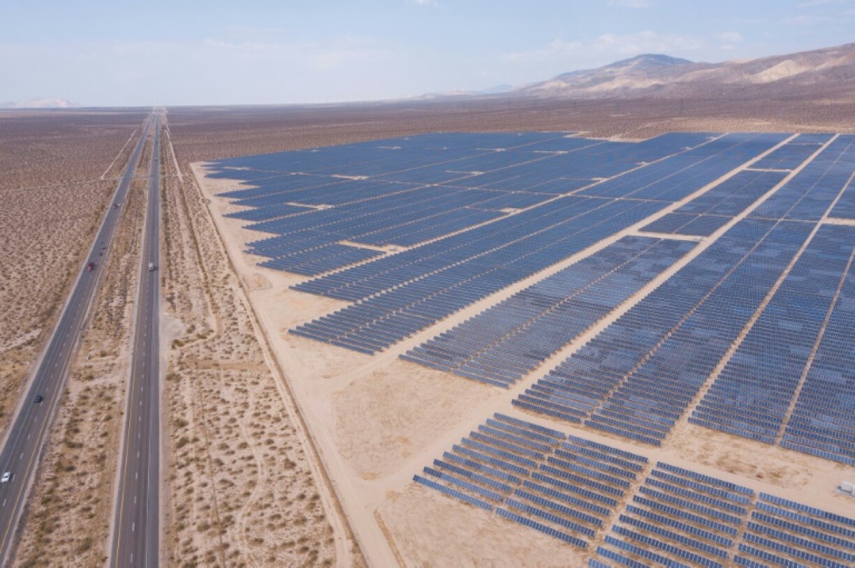 An aerial image shows vehicles driving on the California 14 Highway as solar panels, part of an electricity generation plant, stand on June 18, 2021 in Kern County near Mojave, California