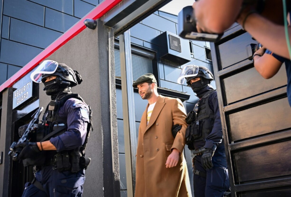 Tristan Tate (c), frère de l'influenceur britannique Andrew Tate, escorté par des gendarmes roumains après une descente de police dans leur résidence, le 21 août 2024 à Bucarest