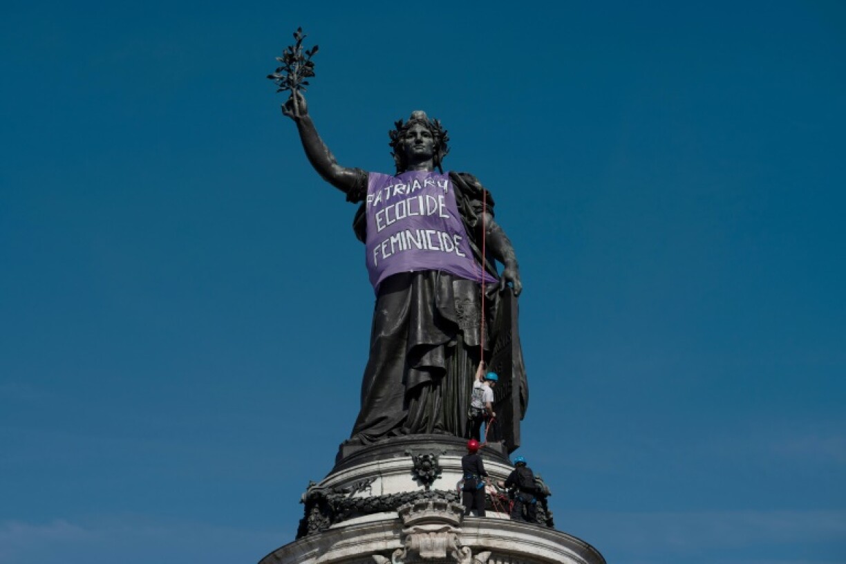 Protesters placing a banner reading 'Patriarchy, ecocide, femicide' on the Statue of the Republic in Paris