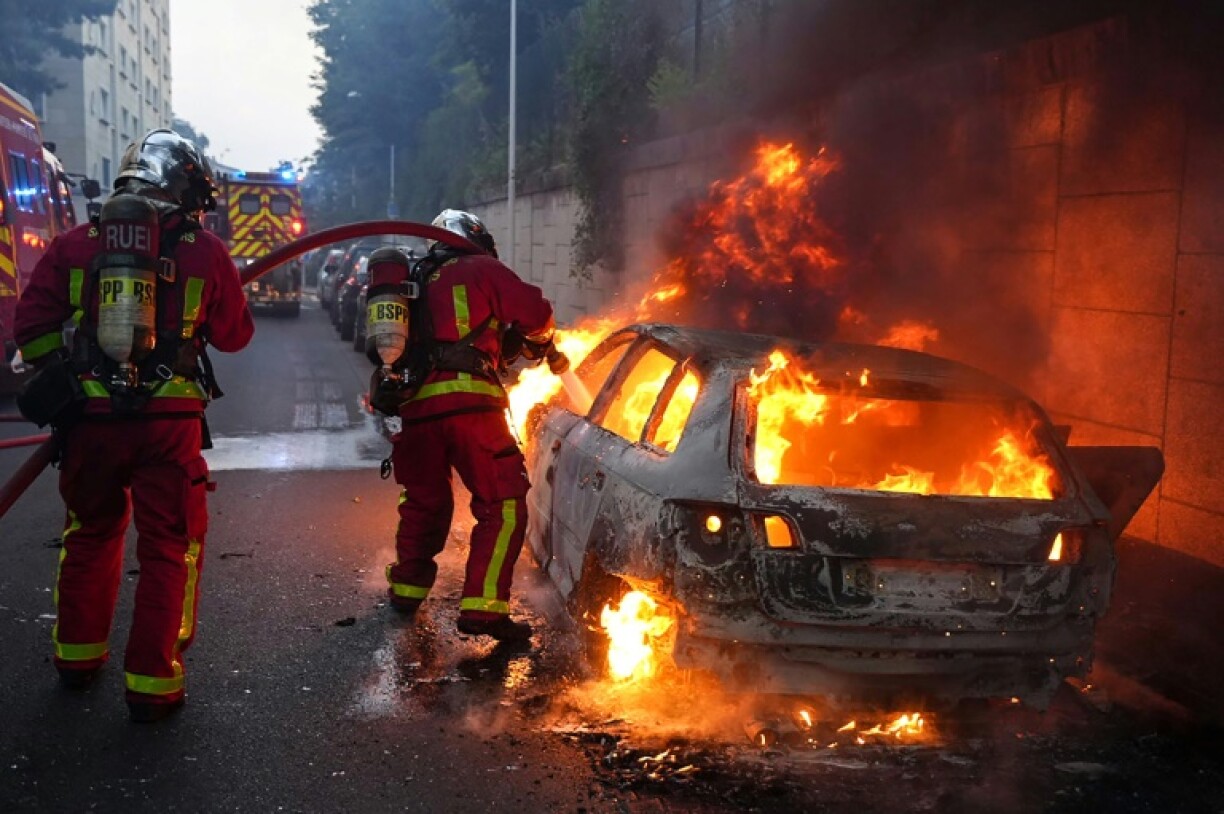 Des pompiers tentent d'éteindre une voiture en feu en marge d'une manifestation à Nanterre, théâtre d'incidents en soirée, le 27 juin 2023