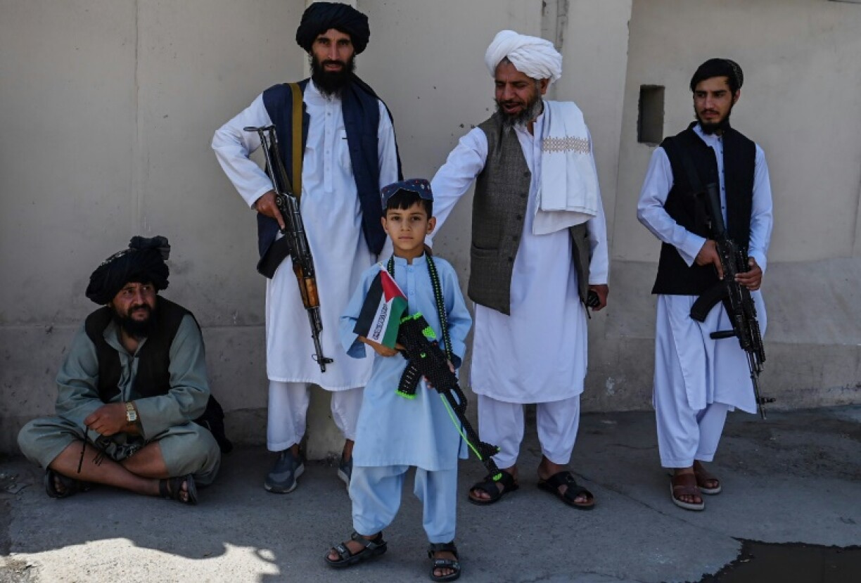 An Afghan boy holding a toy gun looks on as Taliban security personnel stand guard during an anti-Israel protest after the Friday prayers in Kabul