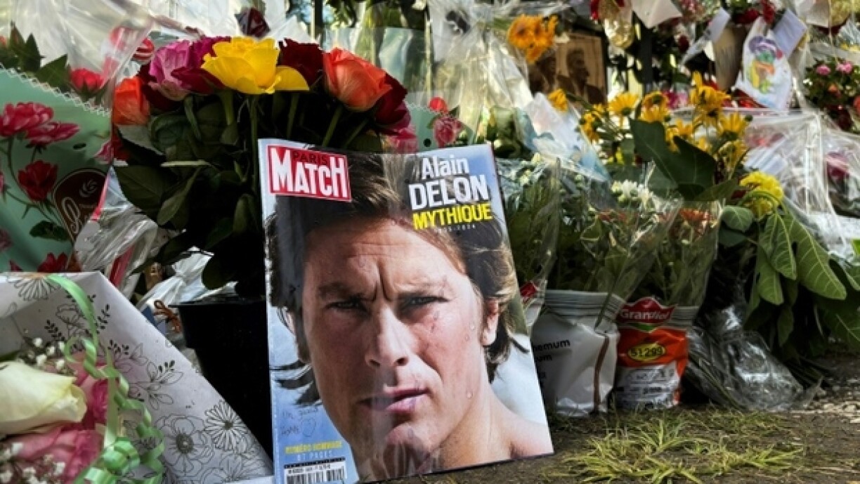 Un portait d'Alain Delon en Une du magazine Paris Match déposé parmi les fleurs devant la propriété de l'acteur décédé, le 21 août 2024 à Douchy, dans le Loiret