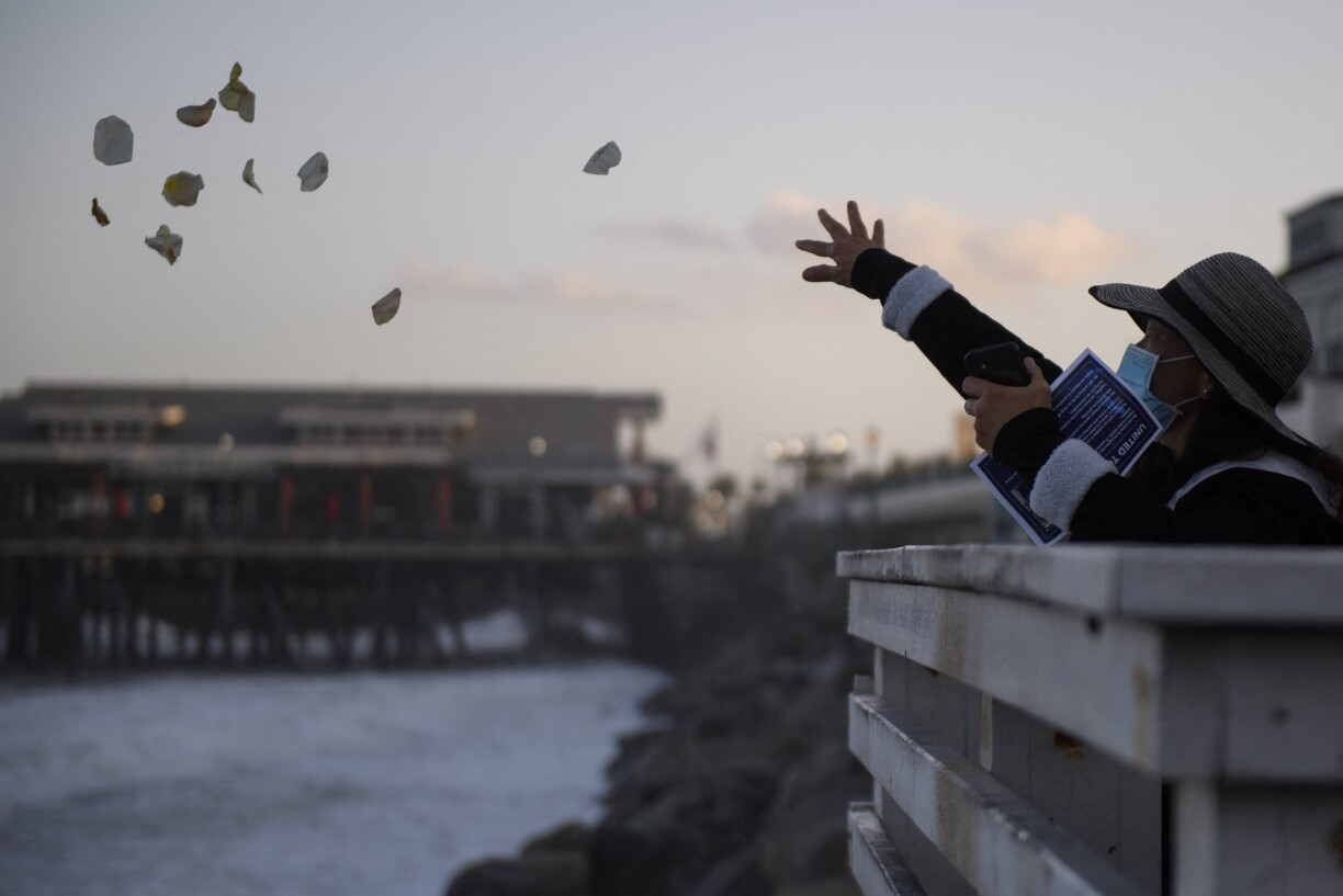 People throw rose petals into the Pacific Ocean during a sunrise vigil organized by United Nurses Associations of California/Union of Health Care Professionals (UNAC/UHCP) at the Redondo Beach Pier to remember health care workers and patients who died from the Covid-19 pandemic on May 22, 2021 in Redondo Beach, California.
