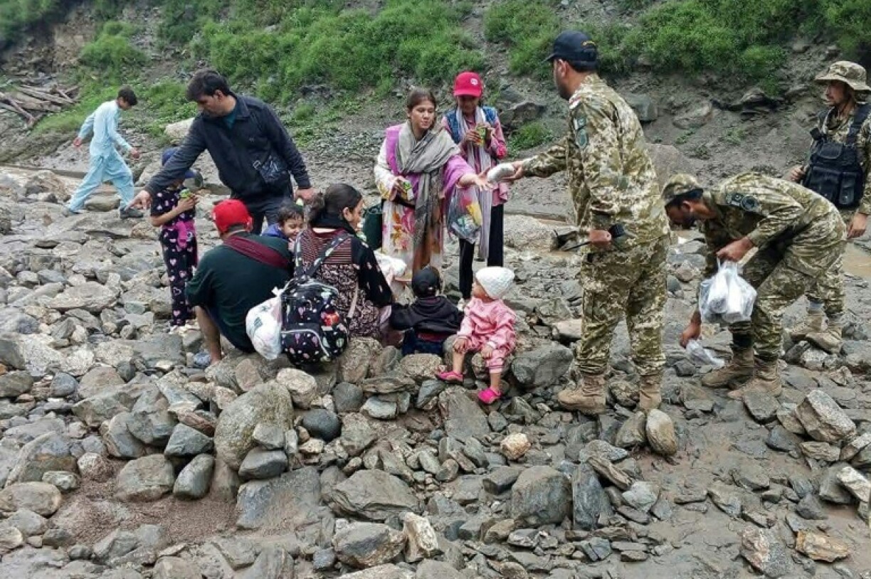 Rescued families holding babies and carrying rucksacks sat on rocks while rescue teams handed them food