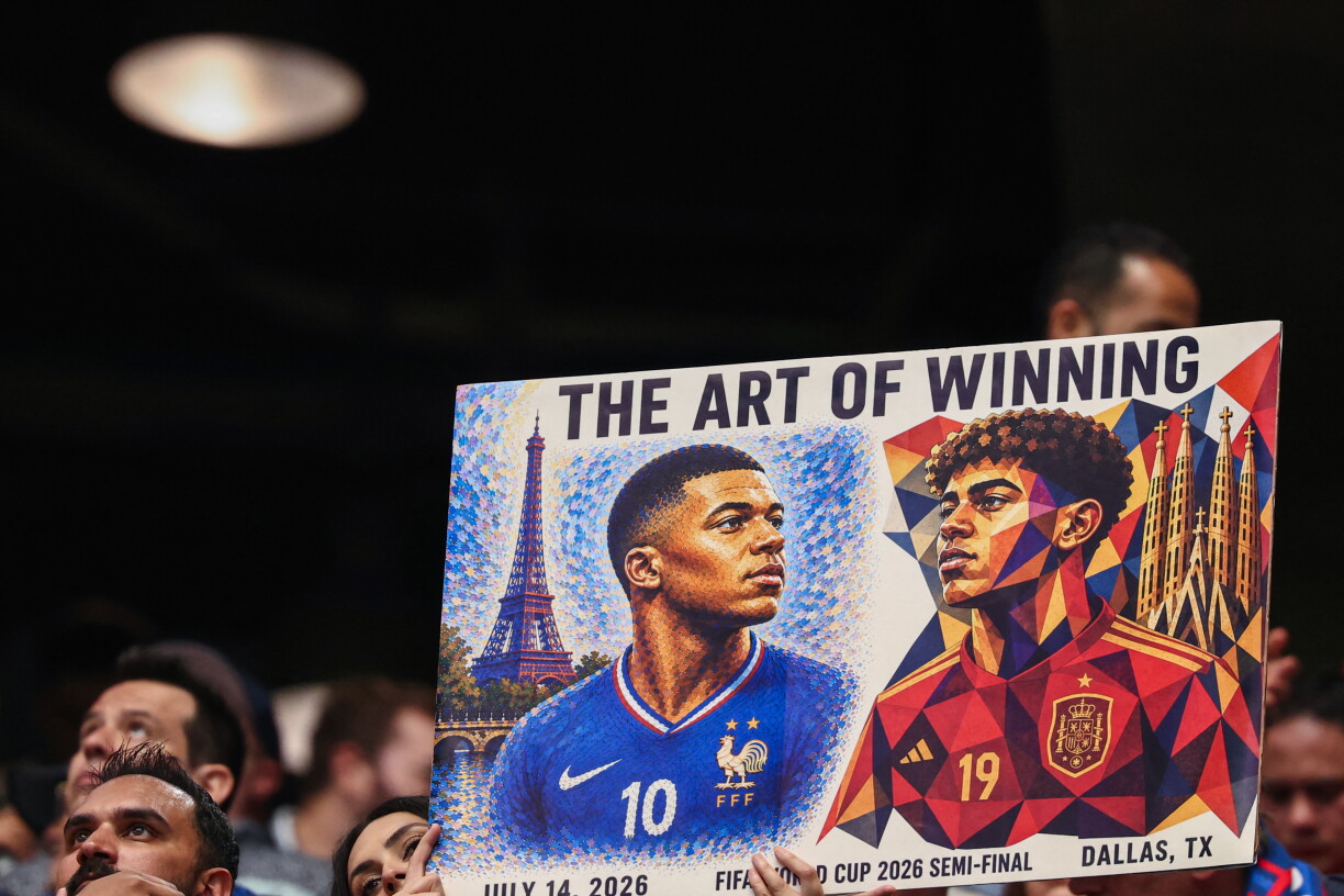 E Fan hält e Schëld an d'Luucht, op deen de Kylian Mbappé virum Eifeltuerm an de Lamine Yamal virun der Sagrade Familia duergestallt ginn.