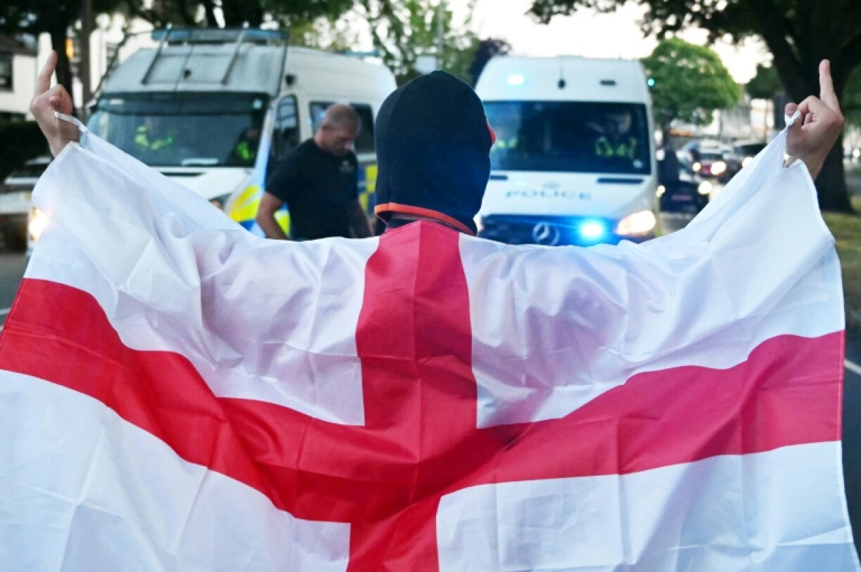 A protester wrapped in the St George flag of England gestures as he stands blocking the road in front of police vehicles in Epping