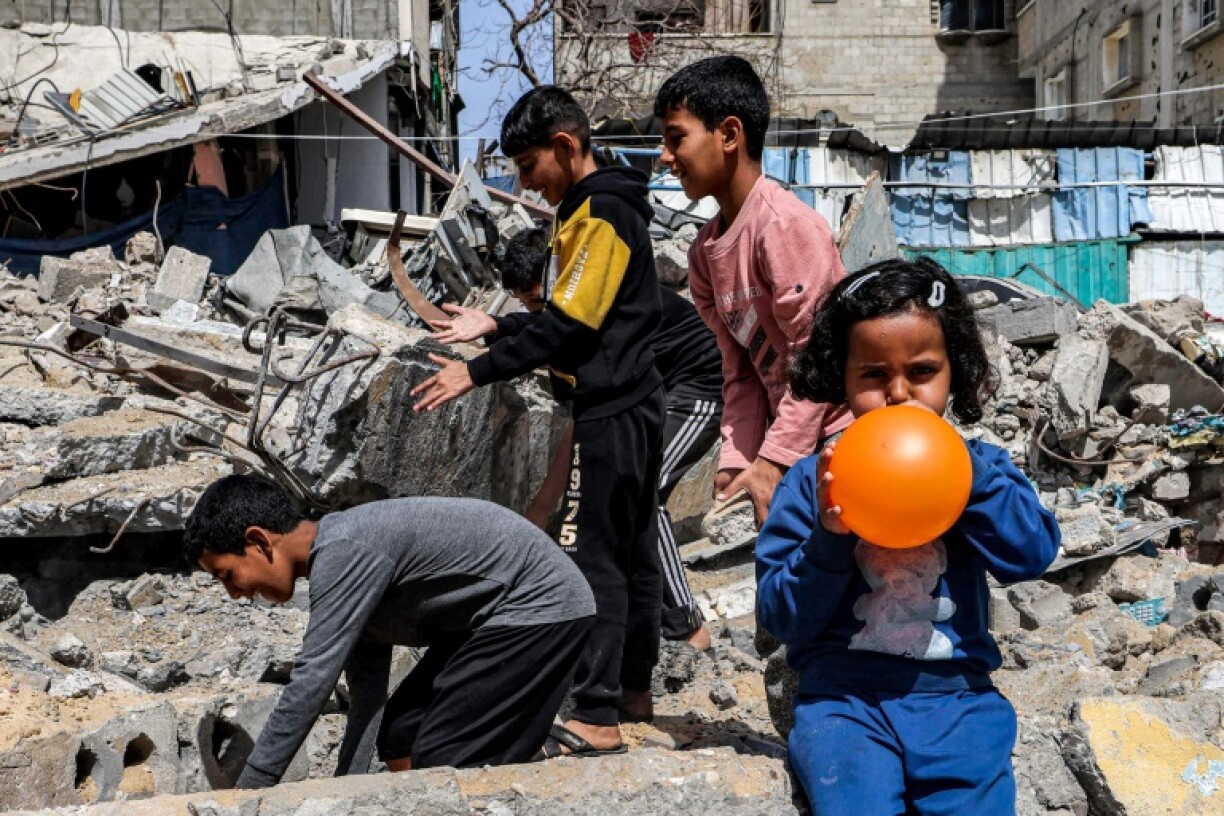 Une petite fille gonfle un ballon pendant que des garçons fouillent les décombres d'un bâtiment détruit à Rafah, dans le sud de Gaza, le 5 avril 2024