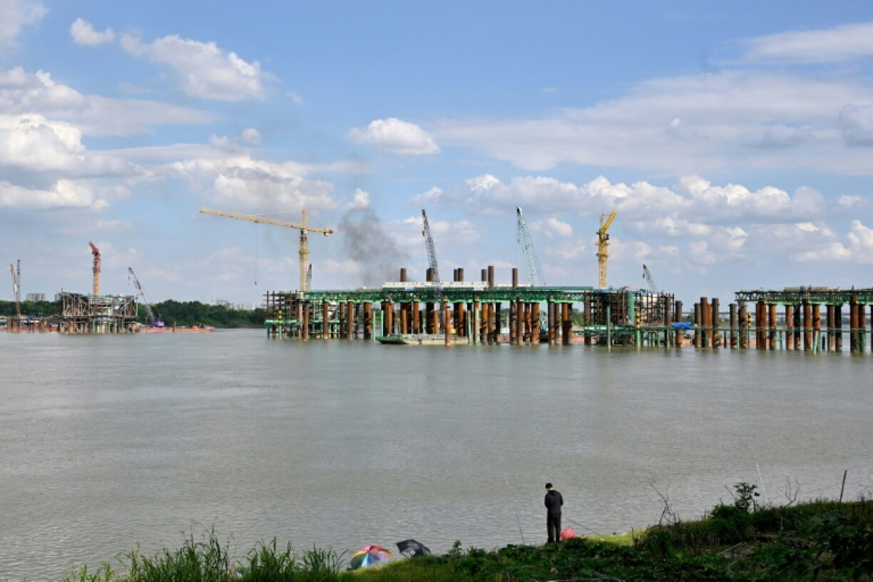 A man fishes along the banks of the Red River near the construction site of the Tran Hung Dao Bridge in Hanoi