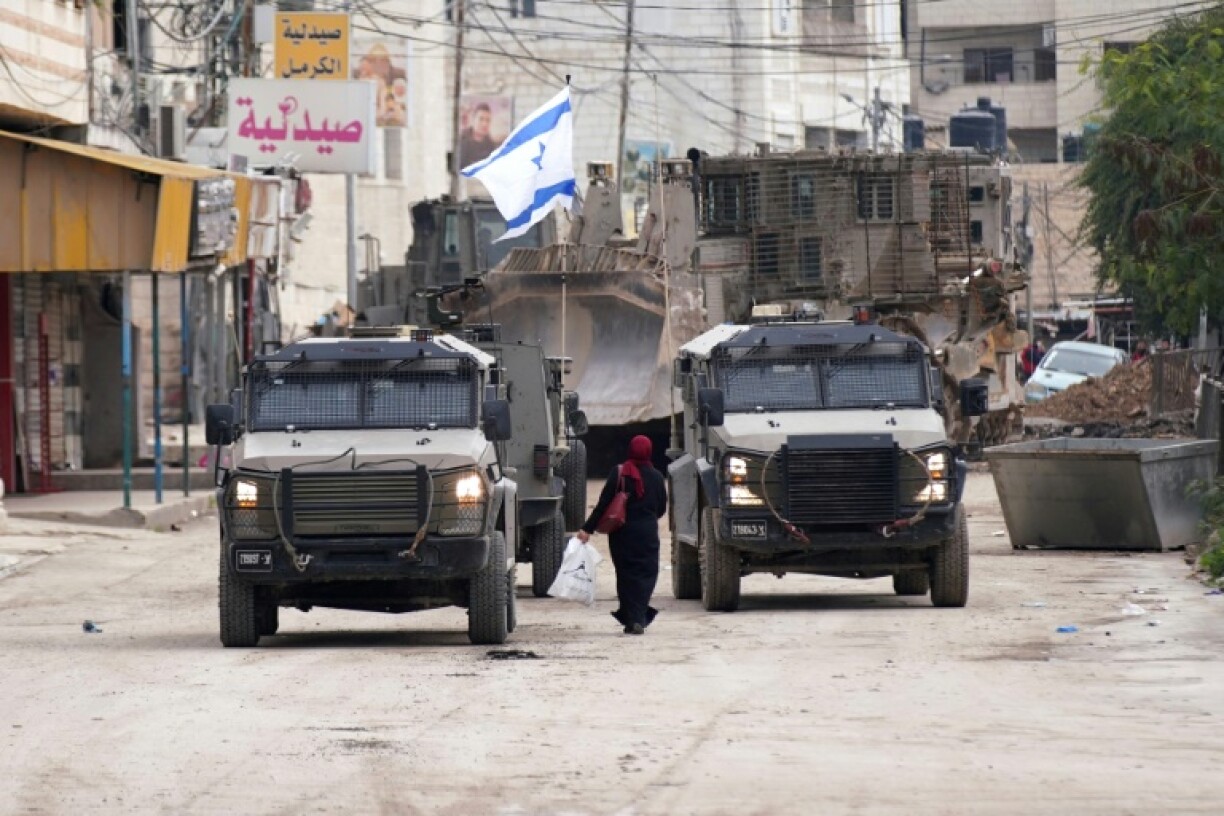 A Palestinian woman walks past Israeli army vehicles during a military raid in Jenin in the occupied West Bank
