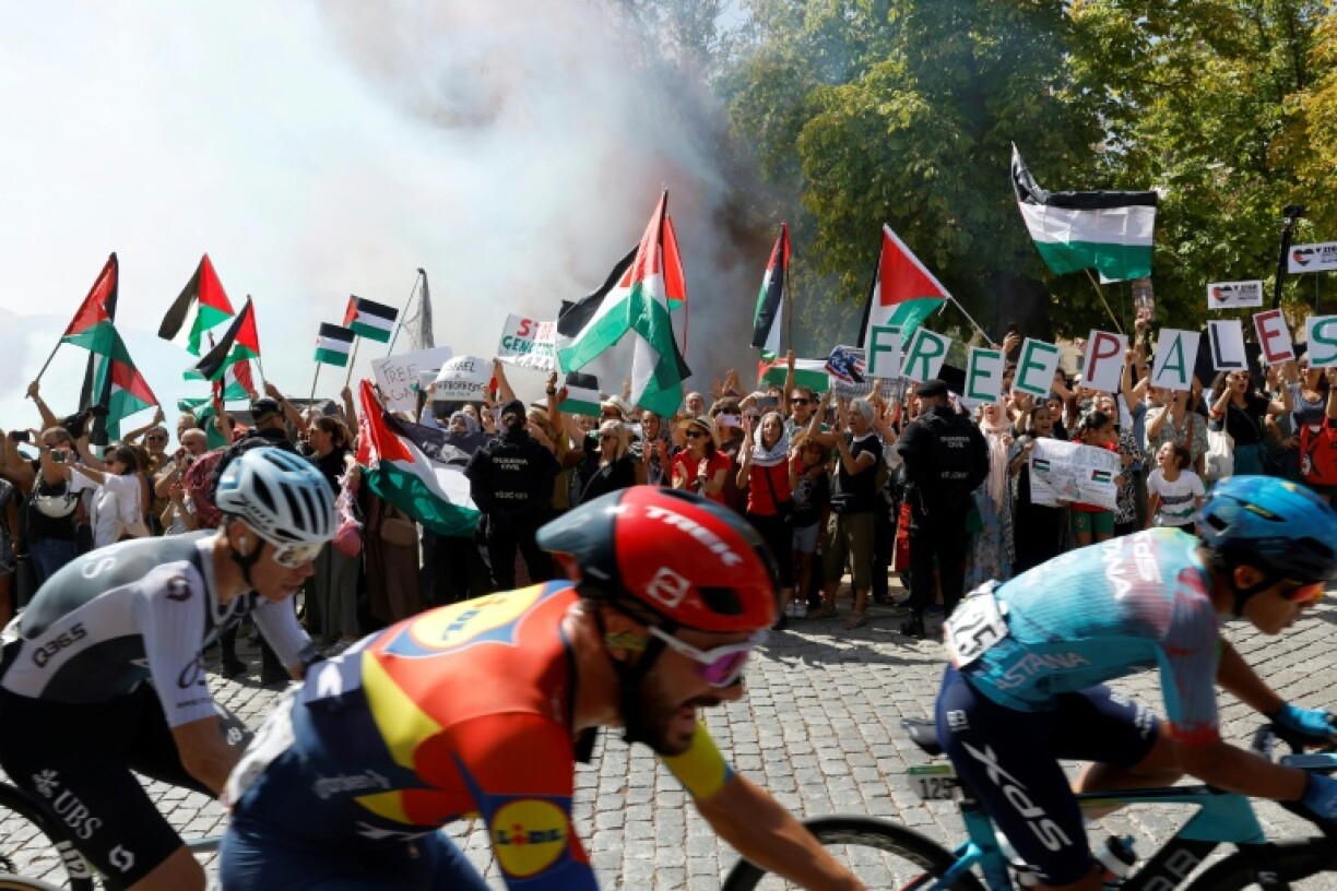 The pack rides in front of pro-Palestinian protesters during the 20th stage of the Vuelta a Espana on September 13, 2025