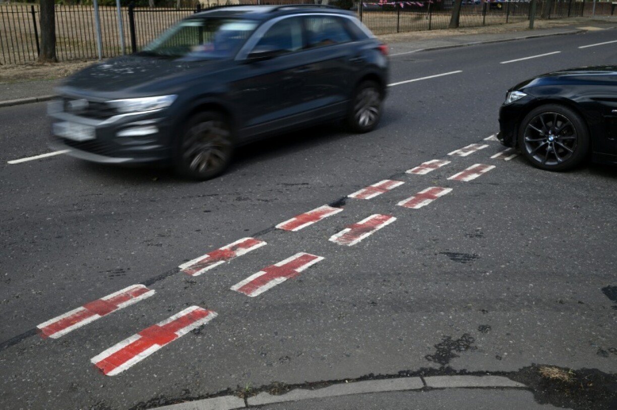 Cars pass St George's Cross flags, the national flag of England, painted onto the white of the road markings near a London residential street
