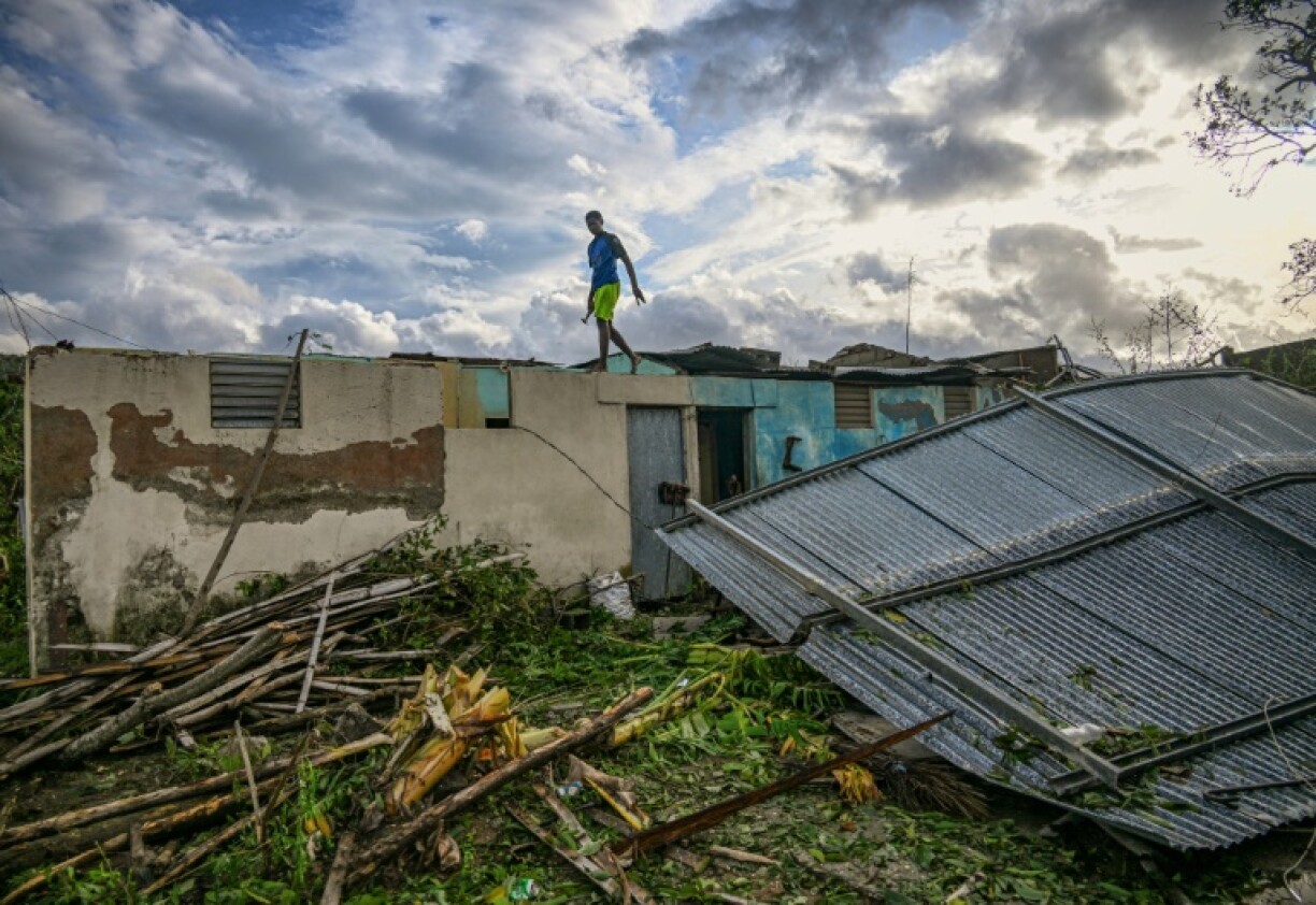 Un habitant de la ville d'El Cobre, dans la province de Santiago de Cuba, marche sur le toit de sa maison endommagée après le passage de l'ouragan Melissa, le 29 octobre 2025.